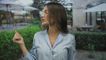Fototapeta premium Woman wearing eyeglasses and striped shirt palm up gesture at restaurant building terrace; contemplation.