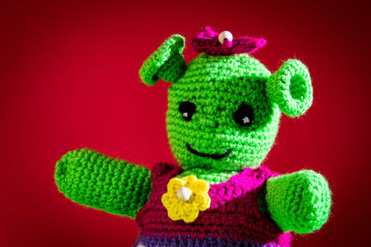 Mu&ntilde;eca verde de ganchillo, ogra simp&aacute;tica con fondo rojo