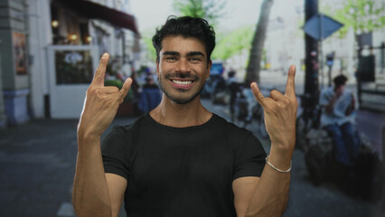 Man with a broad smile shows rock horns with both hands on a city street amid blurred bicycles and buildings  excitement fun metal. © Krakenimages.com