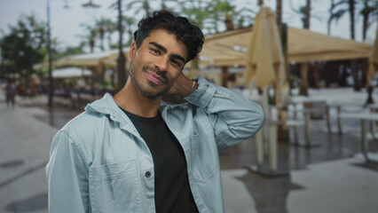 Man wearing denim shirt running hand through hair on outdoor restaurant terrace under umbrellas; relaxation.