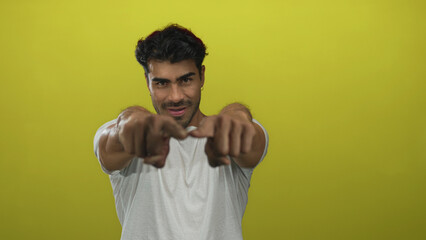 Naklejka premium Man points finger to viewer in yellow studio environment, gesturing directly toward camera; confidence connection engagement.