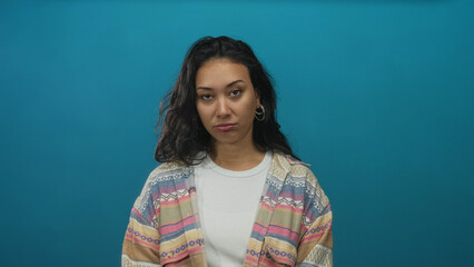 Fototapeta premium Young woman face glances up in studio against smooth teal backdrop wearing patterned cardigan; skepticism doubt contemplation.