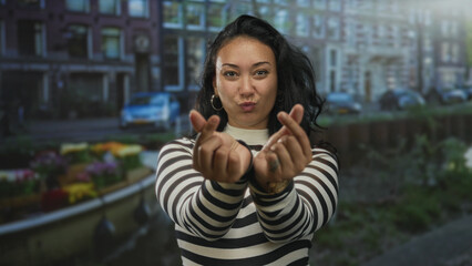 Woman smiling, hands forming finger heart gesture on amsterdam canal street near water and boat, striped sweater and hoop earrings visible  playful affection. © Krakenimages.com