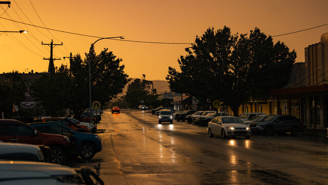 Cars driving along street in heavy rain during vibrant sunset