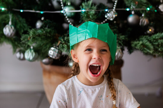 Australian child sitting under Christmas tree wearing green paper cracker hat and smiling