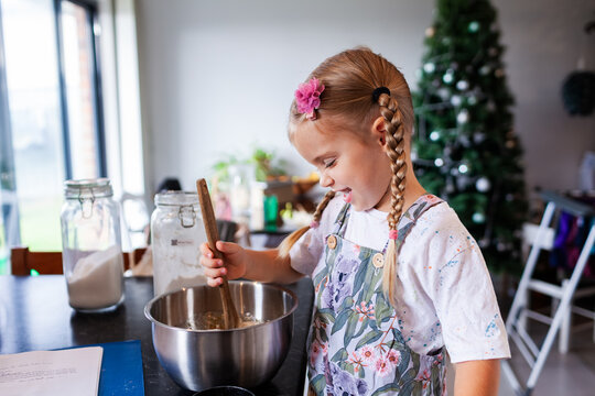 Happy pre-schooler child in kitchen at home mixing biscuit batter in bowl