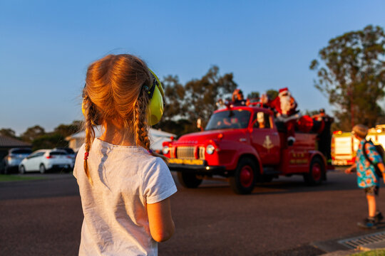 Little girl with earmuffs waving to santa on fire truck on lolly run at Christmas time