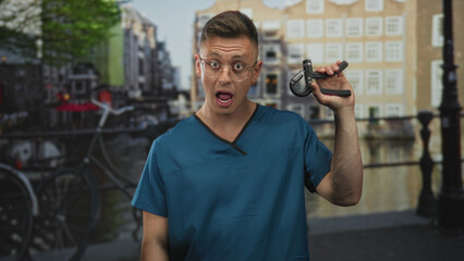 Man physiotherapist in blue scrubs holds a hand gripper aloft with raised hand, mouth open in...
