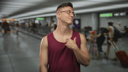 Obraz premium Man tugs shirt at chest and smirks in airport concourse amid moving travelers and luggage; confidence swagger.