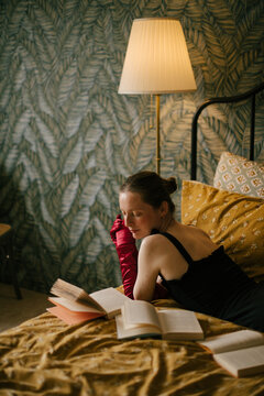 Elegant woman with frecklesin black dress and red gloves reading book in vintage interior with warm light.