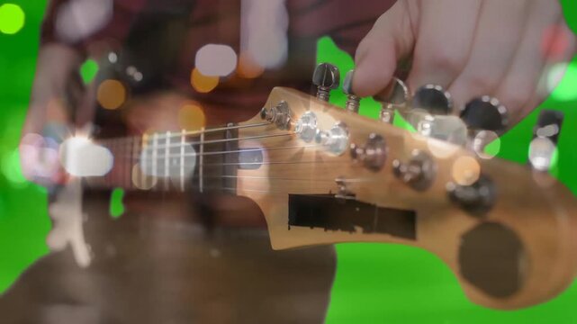 male hand adjusting guitar headstock in music studio, featuring bokeh and green chroma backdrop