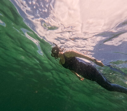 Underwater form below Woman in wetsuit snorkelling in ocean with cloudy sky visible
