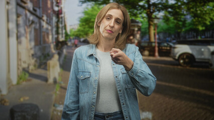 Fototapeta premium Woman points index finger to temple and gestures with other hand, denim jacket and parked car visible on street; thoughtful reflection.