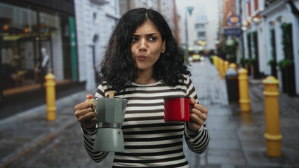 Young woman holding a moka pot and red mug on a cobbled city street, puckering and tasting hot...