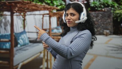 Fototapeta premium Woman young brunette wearing headset pointing finger on street near outdoor patio seating and pergola; skeptical expression.