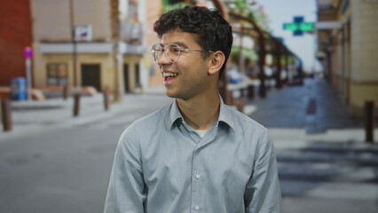 Obraz premium Man wearing glasses and blue shirt laughs showing white teeth on a sunlit street by a building outdoors; joy.