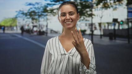 Fototapeta premium Woman points finger and makes peace sign on city street wearing striped blouse, hands visible and facing camera; confidence.