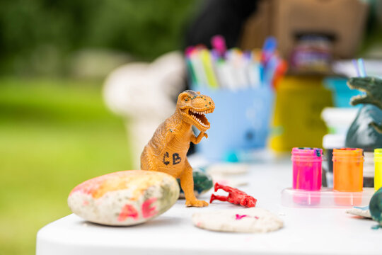 A toy T-Rex dinosaur sits among craft supplies at a child's table at summer camp 