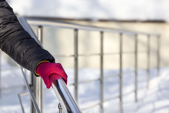 A woman descends the stairs holding onto the railing in winter. A woman holds onto a metal handrail in winter. a woman descends a slippery staircase. safety in winter. 