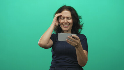 Woman holding smartphone, hand to forehead while smiling and laughing in studio; joy laughter connection.