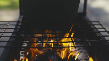 the pot stands on a burning fire, cooking on a camping trip, cooking in a fire pit in nature, outdoor activities, lighting a fire, delicious travel recipes, adventure season, slow motion. © TO LOVE