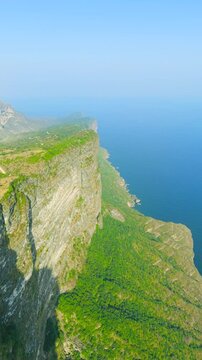 Aerial view of massive limestone cliffs dropping into the Arabian Sea with green vegetation along the coast near Salalah, Oman.