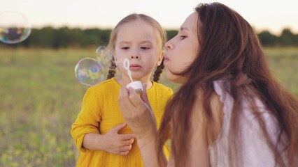 Fototapeta premium young mother blowing soap bubbles with little girl daughter. happy family. fun family bubble blowing game. child kid plays with mother soap bubbles park. outside. happy family park outdoor. summer day