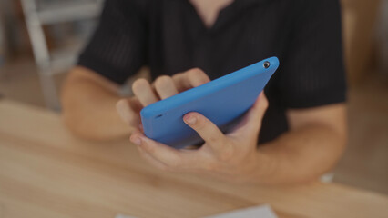 Fototapeta premium Man holding and tapping a blue tablet with fingertips at a wooden table in building, hands visible; focus productivity.