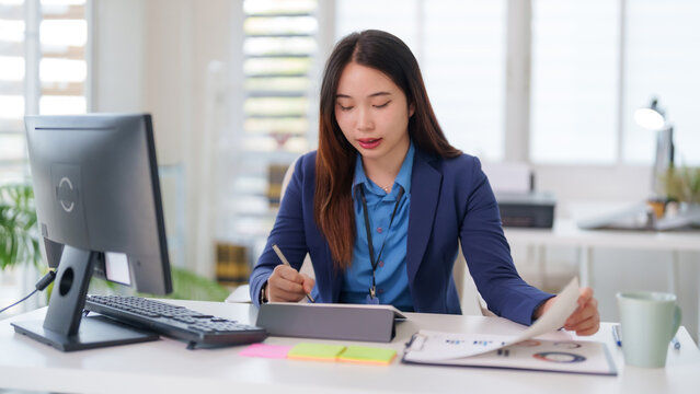 Asian adult business professional woman taking notes digital tablet analyzing business reports modern office desk workplace productivity