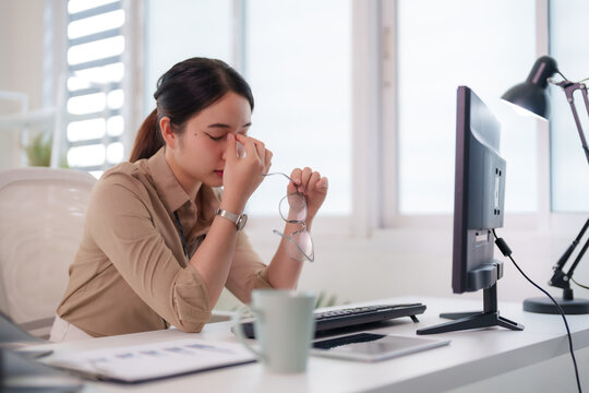 Asian professional woman experiencing eye strain from long computer work at modern bright office business workplace due to digital screen fatigue