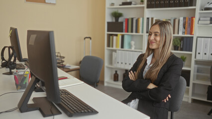 Woman in blazer typing with hands on keyboard at a desktop computer and looking at monitor in an...