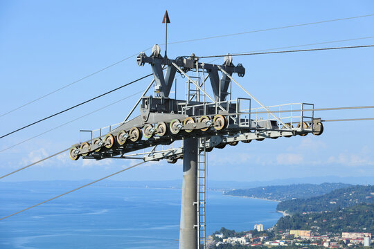 Cable car support tower with pulley wheels. Industrial metal construction stands against blue sea and coastal city landscape