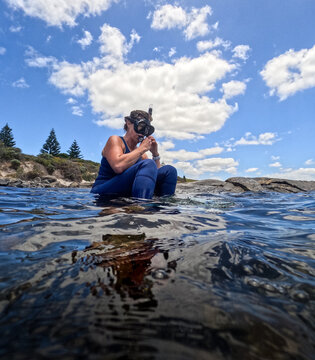 Woman in wetsuit adjusting mask and snorkel ready to snorkel clear ocean water