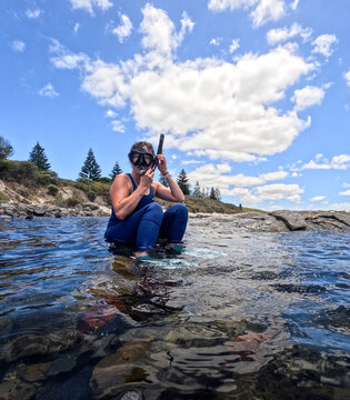 Woman in wetsuit adjusting mask and snorkel ready to snorkel clear ocean water