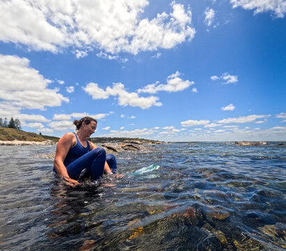 Woman in wetsuit wearing mask, snorkel and fins sitting in clear ocean water preparing to snorkel