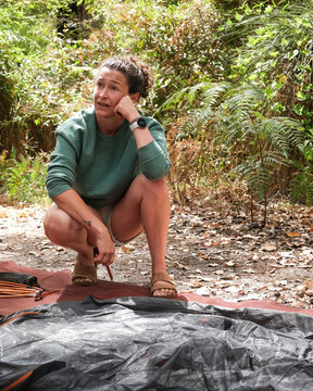 Woman building and constructing camping tent in forest surrounded by large trees in summer weather