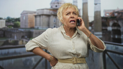 Fototapeta premium Woman holding smartphone to ear, hand on hip and gesturing on balcony by historic building; frustration urgency.