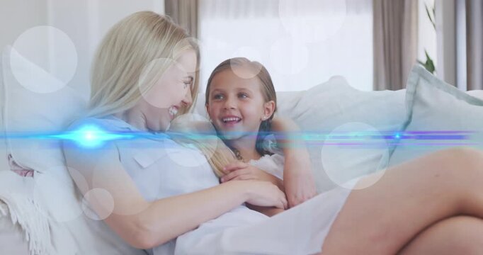 Animation of light and dots moving over happy caucasian mother and daughter talking on sofa