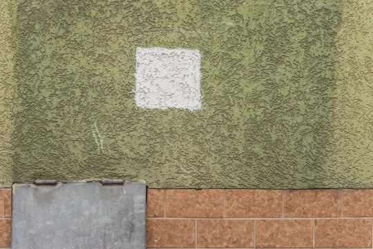 Detail einer gr&uuml;nen Hausfassade mit weissem Quadrat (Farbmuster), Teil einer Stahlklappe und braunen Kacheln