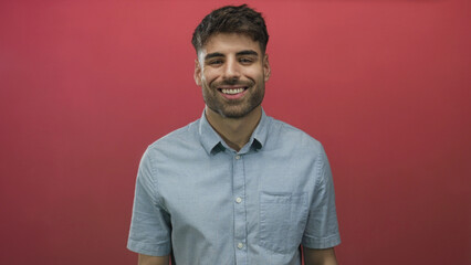 Obraz premium Young hispanic man smiling with teeth in red studio wearing light blue shirt; confidence joy optimism cheerful.