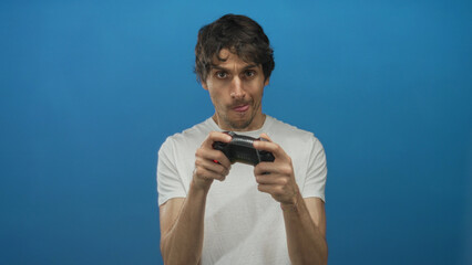 Man wearing white t-shirt holds gamepad controller with tongue out while raising one hand in studio  focus challenge energy fun. © Krakenimages.com