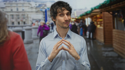 Man steeples fingers while surveying bustling street market stalls during daytime; confidence...