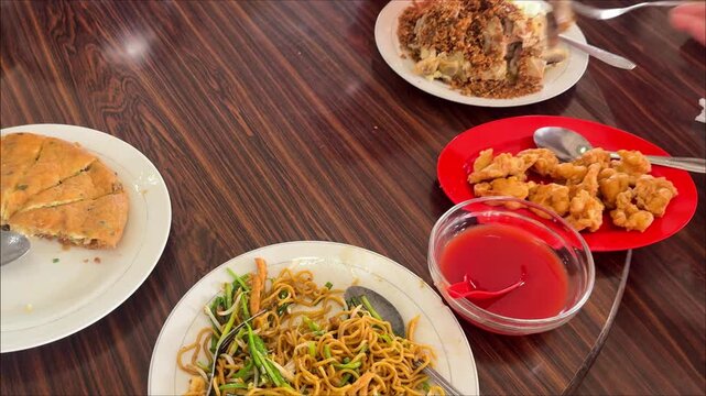 Chinese restaurant table scene featuring chow mein fried noodles, egg foo young, fried shrimp or prawn  and steamed chicken with fried garlic on top served on a rotating wooden table.