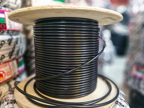 Coiled black electrical cable rolls displayed inside a hardware store, showing industrial wiring supplies ready for installation. Concept of electricity, construction materials, equipment storage, and