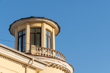 Architectural detail of a round turret with large windows and a decorative balcony on a yellow building against a clear blue sky © Denis Tuev