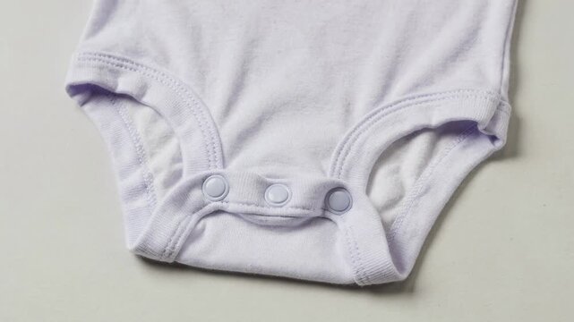 Medium shot of baby bodysuit with plastic snap closures on the crotch highlighting smooth finish and gentle fabric binding for infant comfort and convenience.