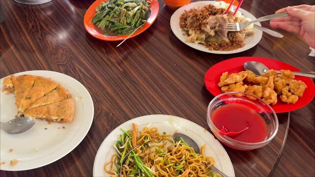 Chinese restaurant table scene featuring chow mein fried noodles, egg foo young, fried shrimp or prawn  and steamed chicken with fried garlic on top served on a rotating wooden table.