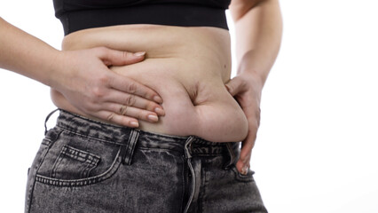 Naklejka premium Woman pinching and pulling her abdominal skin, showing visible body changes. Weight loss, fitness, and healthy lifestyle concept.