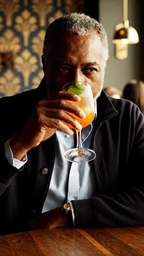 Smiling man enjoys cocktail in upscale bar. Vertical shot captures sophisticated atmosphere and warm vibe. Relaxing moment shared with friends during evening.