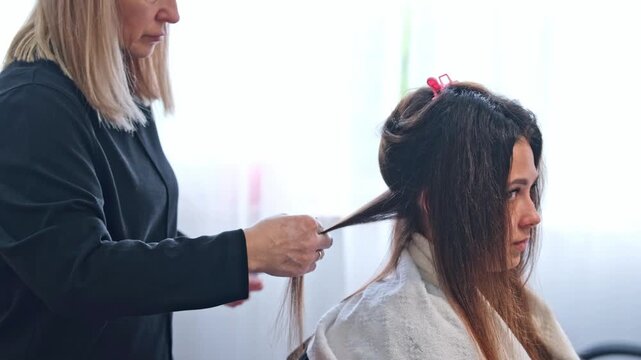 A hair stylist applies keratin hair treatment to smooth and straighten hair. The stylist carefully brushes and styles the client's hair. This process takes place in a beauty salon setting.